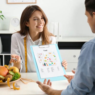 Young nutritionist consulting patient at table in clinic